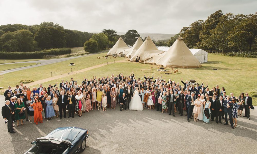 Aerial view of the full wedding group gathered with the couple in front of the Smedmore House estate and tipi marquees