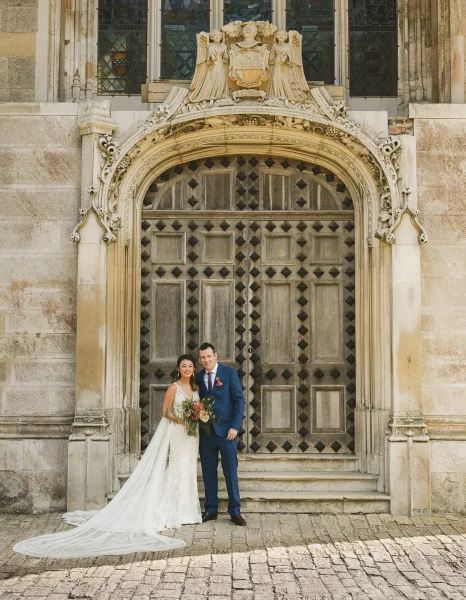 Bride in a cathedral-length gown and groom standing before the ornate Gothic entrance of Highcliffe Castle