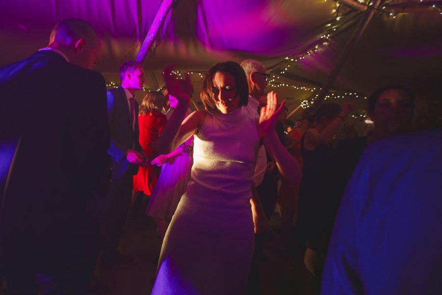 Bride dancing with guests under purple lights and fairy lights inside the tipi marquee at a Smedmore House evening reception