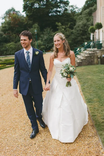 Bride and groom walking happily along the gravel path beside Highcliffe Castle, bride holding a white bouquet