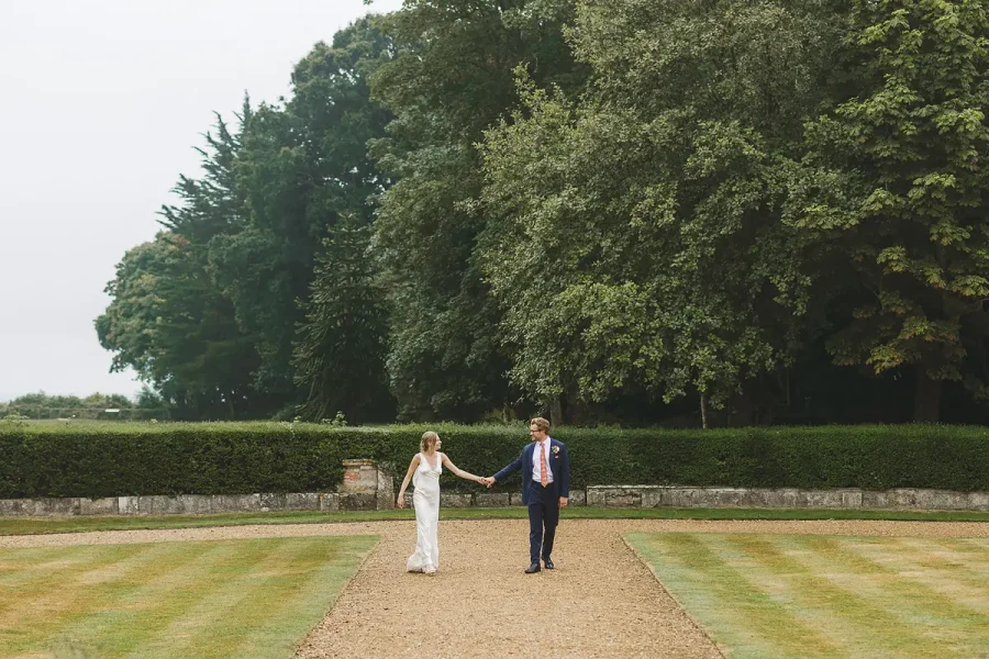 Bride and groom walking hand in hand through the manicured garden lawns at Highcliffe Castle
