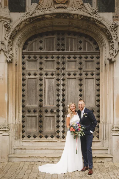 Bride holding a wildflower bouquet and groom smiling together in front of Highcliffe Castle's Gothic doorway