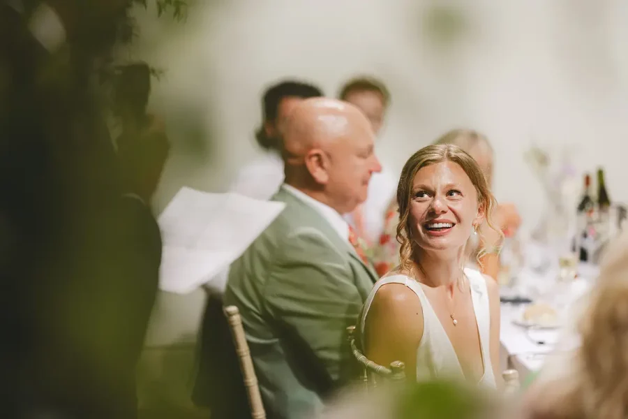 Bride caught laughing at the wedding breakfast at Highcliffe Castle, framed softly by foliage in the foreground