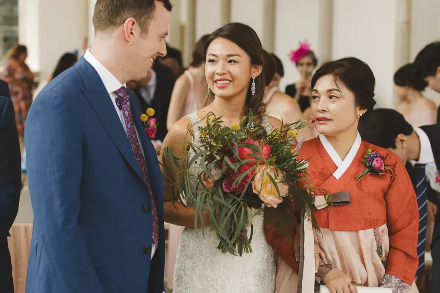 Bride walking to the altar in the Wintergarden at Highcliffe Castle, accompanied by her mother in a Korean hanbok