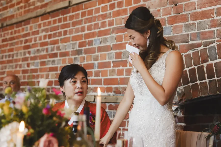 Bride delivering an emotional speech in the Great Hall at Highcliffe Castle, her mother watching beside her