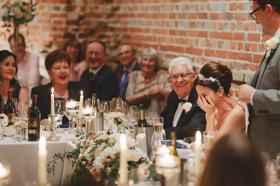 Bride laughing at the wedding breakfast table during speeches at Highcliffe Castle