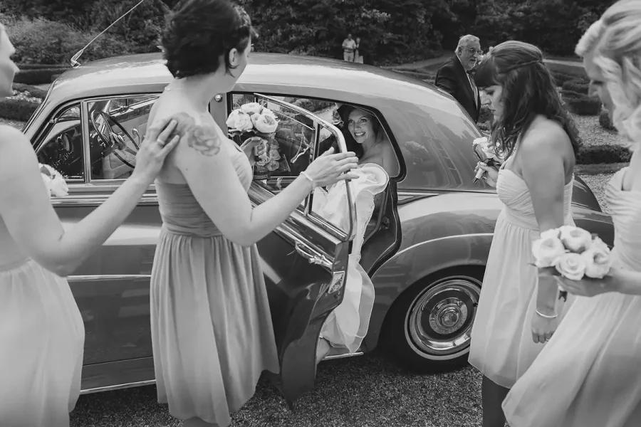 Bride stepping out of a vintage car greeted by her bridesmaids on arrival at Highcliffe Castle