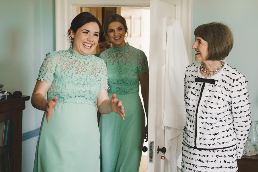 Bridesmaid in mint green dress laughing with the mother of the bride during wedding morning preparations at Smedmore House