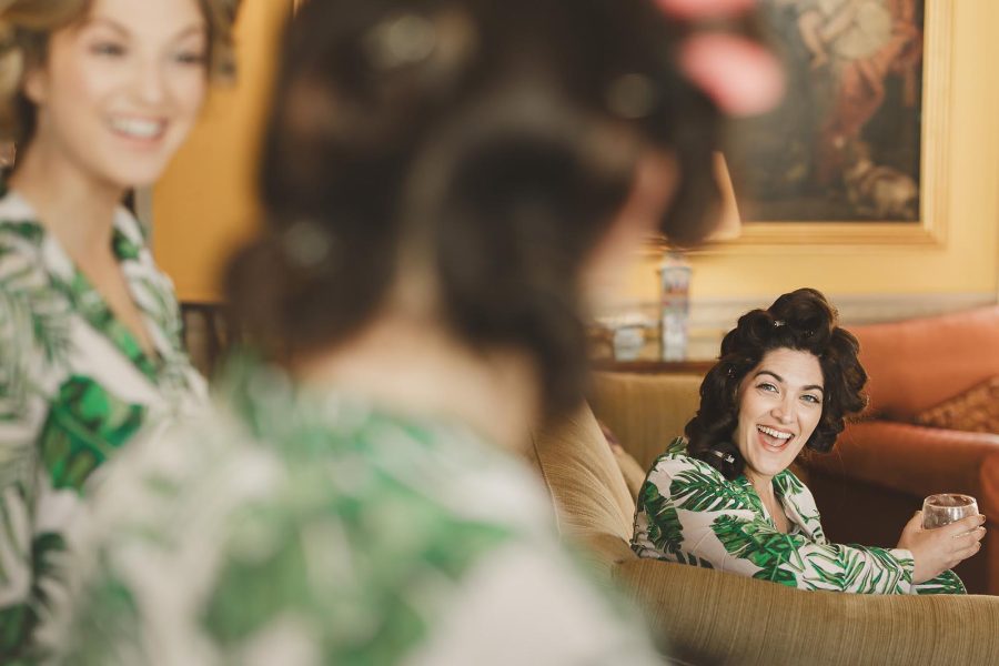 Bridesmaids in matching floral robes laughing together while getting ready inside the warm interior of Smedmore House