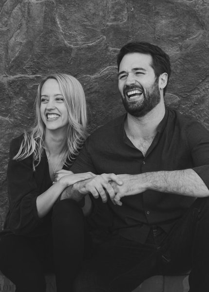 Black and white candid portrait of couple laughing together against a stone wall
