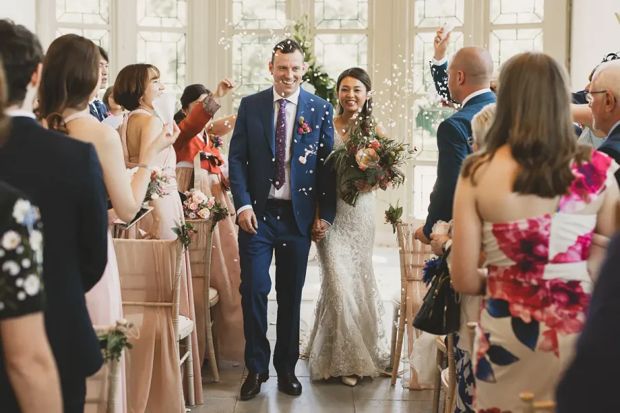 Newlyweds walking through a shower of confetti down the Wintergarden aisle at Highcliffe Castle
