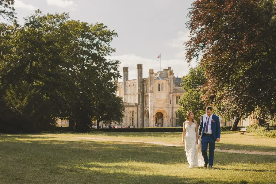 Bride and groom walking across the Highcliffe Castle grounds in warm late afternoon light with the castle behind