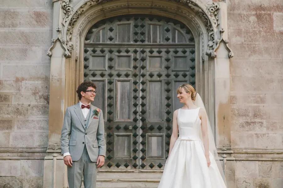 Bride and groom laughing together in front of Highcliffe Castle's carved Gothic entrance doorway