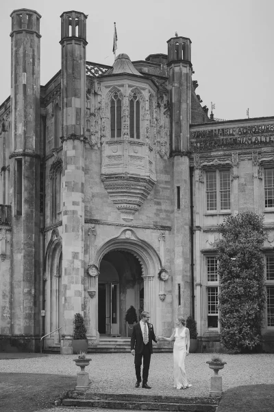 Bride and groom standing before the Gothic tower entrance of Highcliffe Castle, black and white portrait