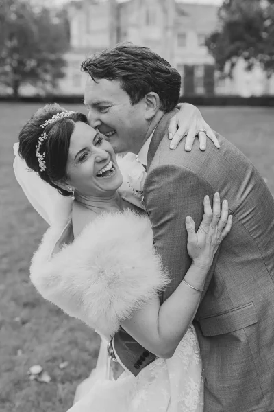 Bride and groom laughing together on the grounds of Highcliffe Castle, the bride wearing a fur stole