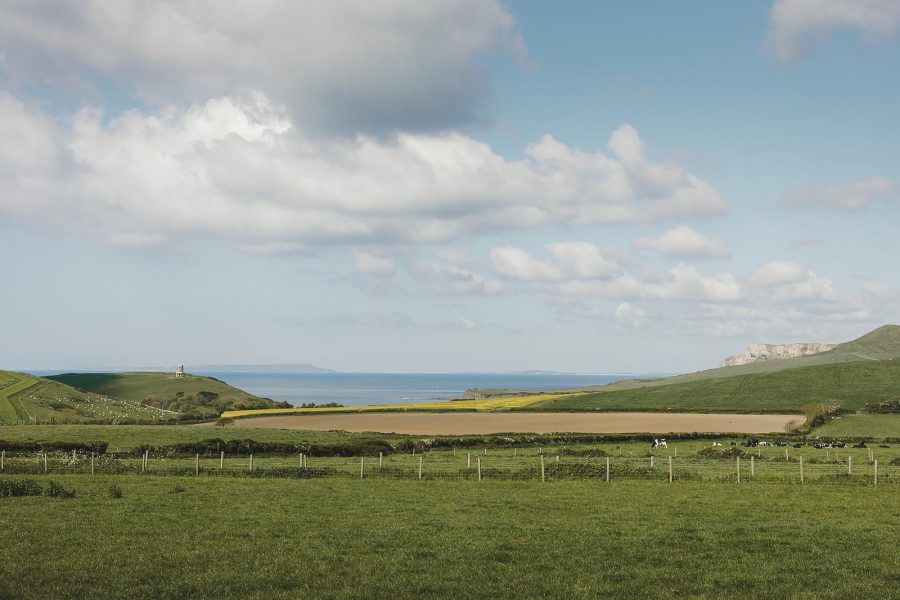 Sweeping Dorset coastal landscape with Clavell Tower on the headland, chalk cliffs and green farmland under a bright sky, Smedmore Estate