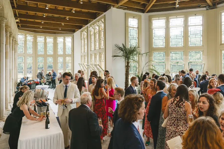 Wedding guests mingling during the drinks reception in the bright, light-filled Wintergarden at Highcliffe Castle