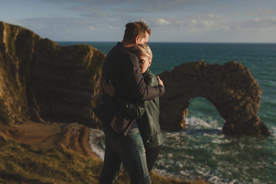 Couple embracing on the cliffs overlooking Durdle Door during a Dorset pre-wedding shoot