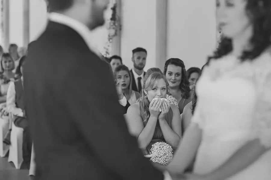 Bridesmaid wiping away tears as she watches the wedding ceremony in the Wintergarden at Highcliffe Castle