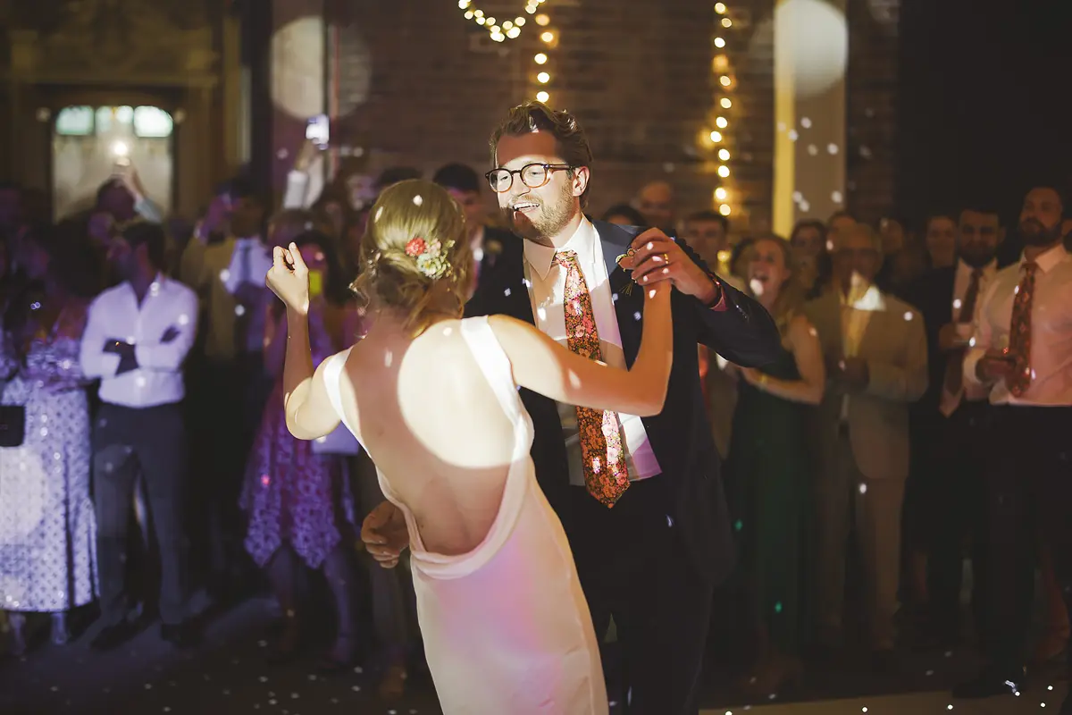 Bride in low-back wedding dress dancing with groom during the first dance with bubbles and fairy lights at Highcliffe Castle