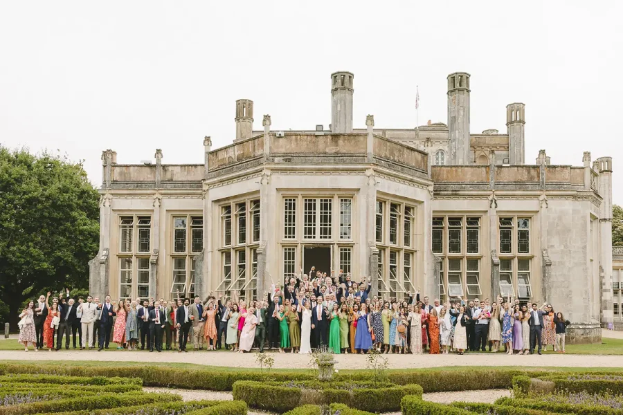 The full wedding party gathered for a group photograph in front of Highcliffe Castle and its formal gardens
