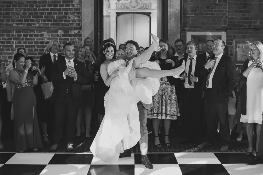 Groom lifting the bride on the chequered dance floor in the Great Hall at Highcliffe Castle as guests cheer