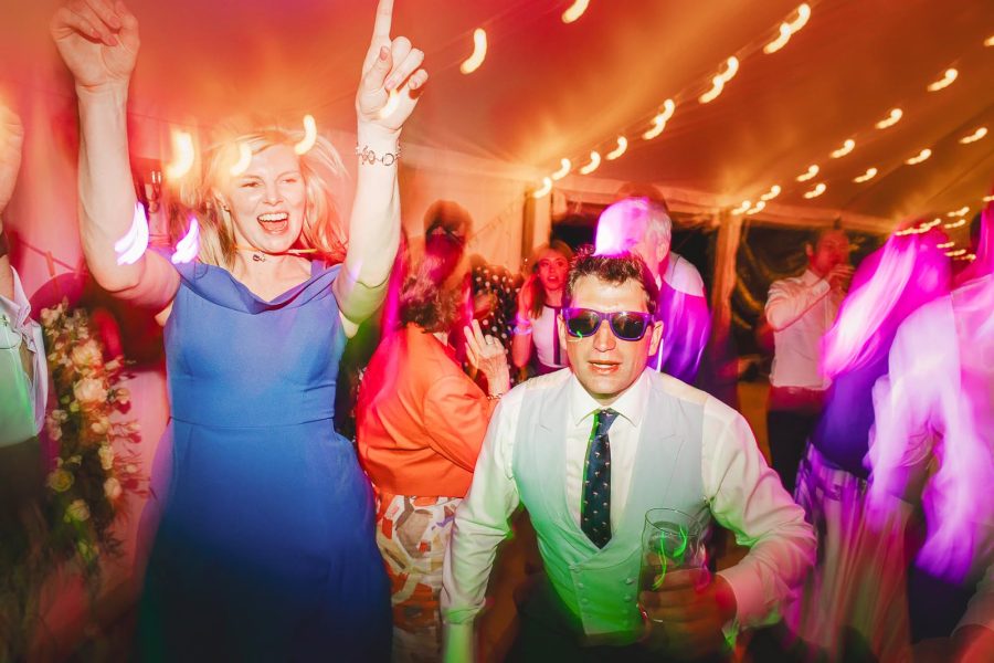 Wedding guests dancing with abandon under pink lights in the marquee at a Smedmore House evening reception