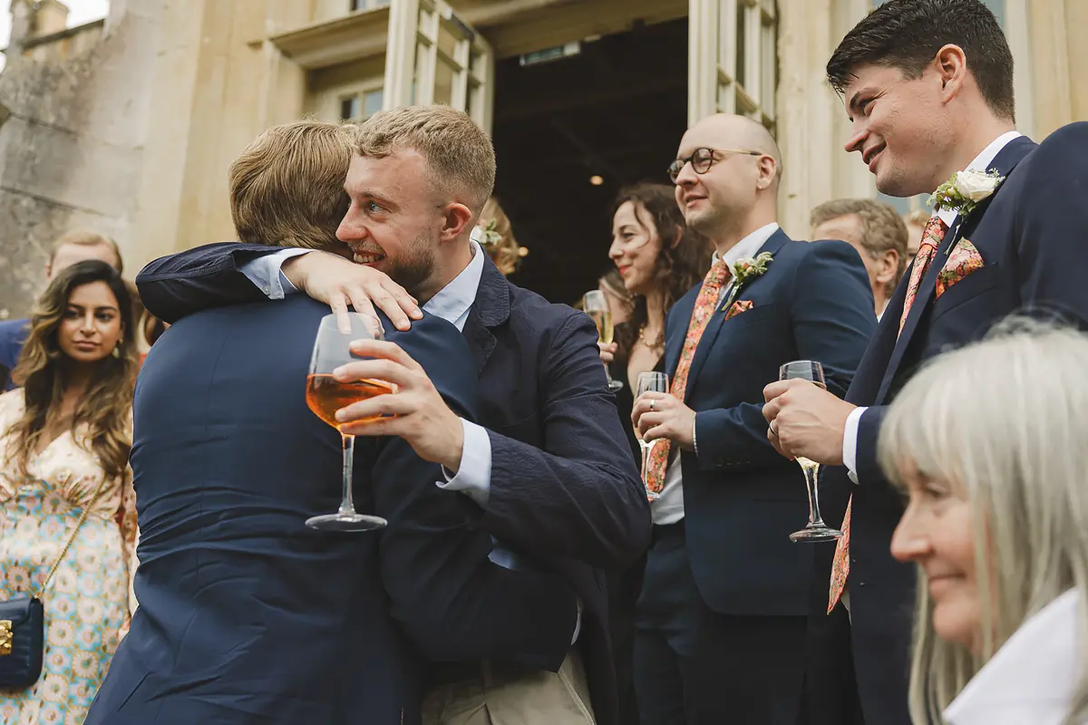 Two male wedding guests sharing a warm hug on the castle steps during the drinks reception at Highcliffe Castle
