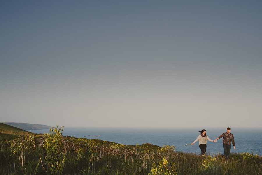 Couple running along coastal cliffs on the Dorset Jurassic Coast during a pre-wedding shoot