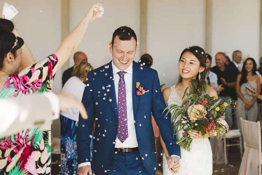 Close-up of bride and groom beaming as confetti rains around them leaving the Wintergarden at Highcliffe Castle