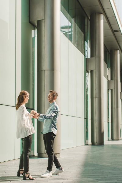 Couple holding hands beside modern architecture during a relaxed portrait shoot