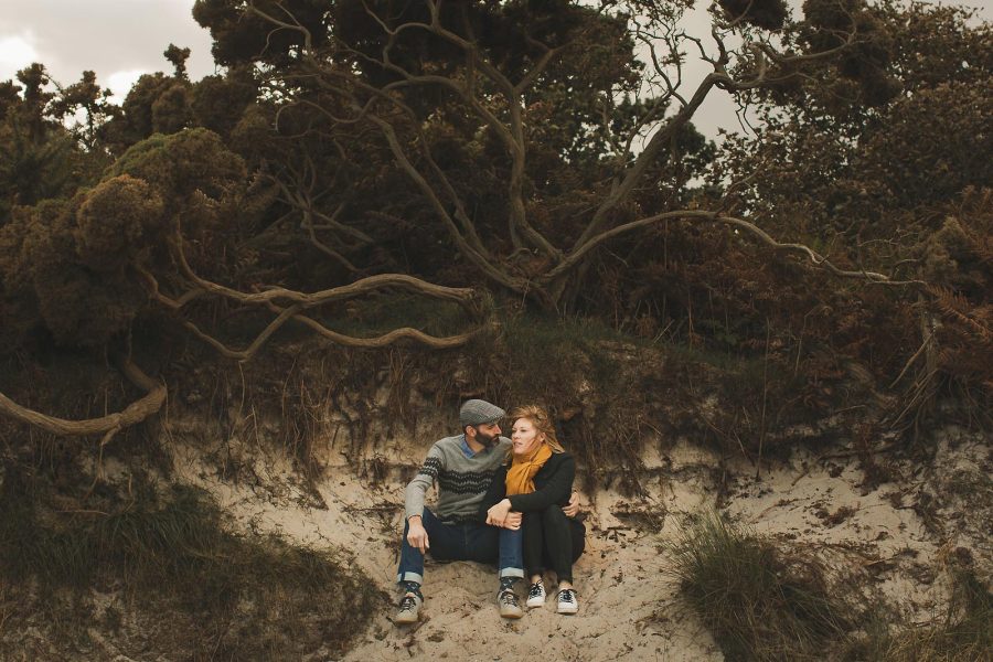 Couple sitting together on sand dunes during a relaxed pre-wedding shoot