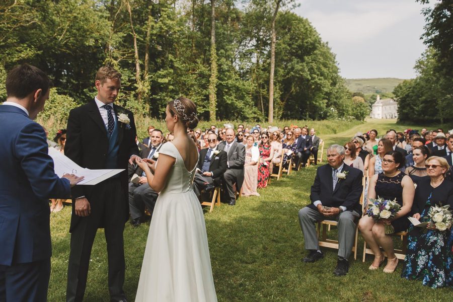 Bride and groom exchanging vows at an outdoor wedding ceremony at Smedmore House with seated guests in rows on the lawn