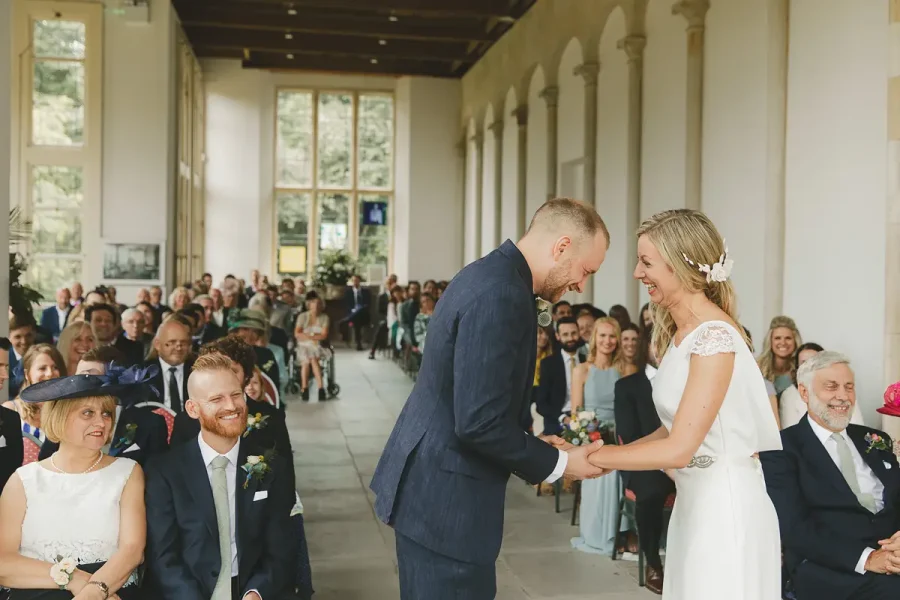 Groom placing the ring on the bride's finger during the ceremony in the Wintergarden at Highcliffe Castle