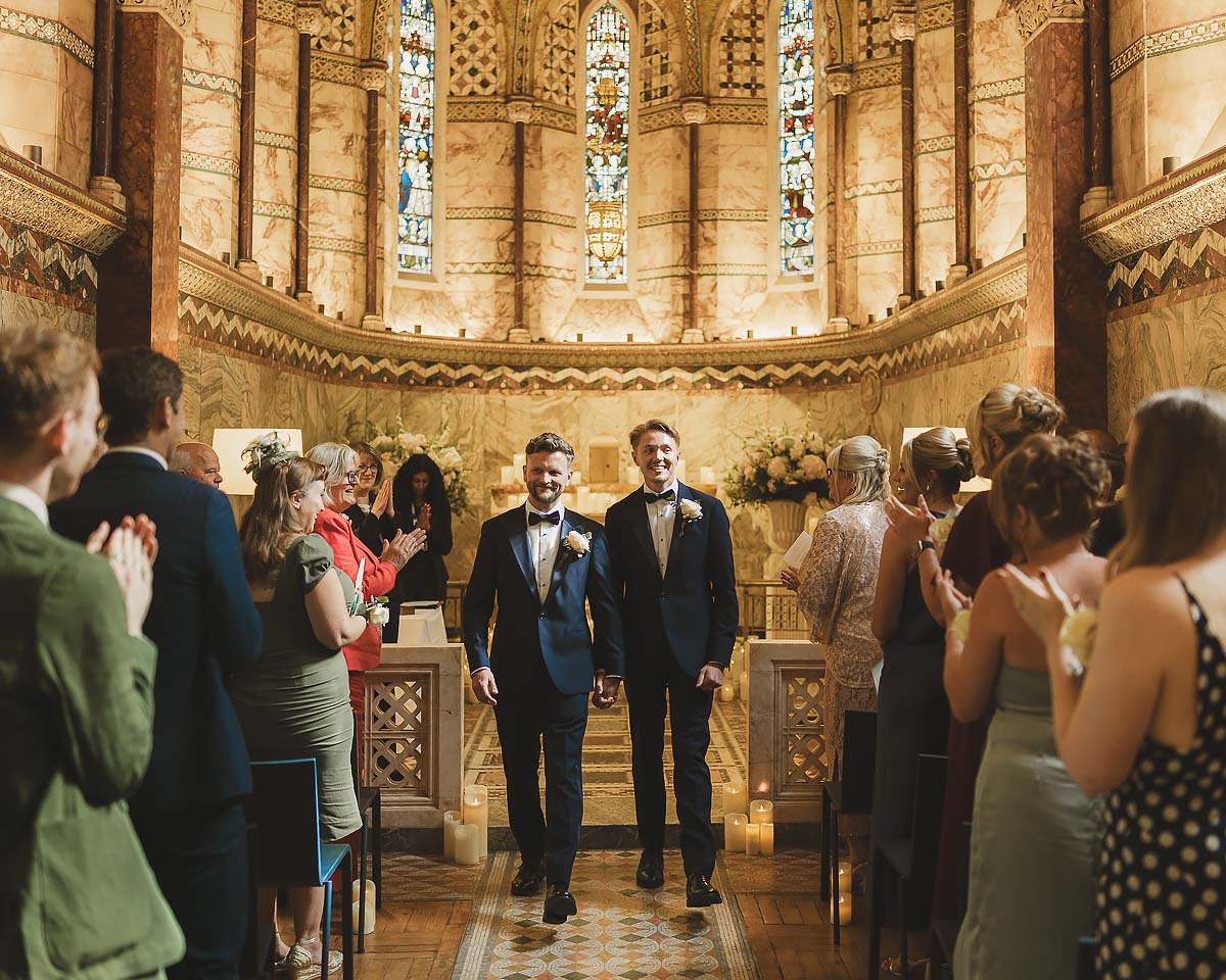 Two grooms walking back down the aisle together during their same-sex wedding ceremony in London