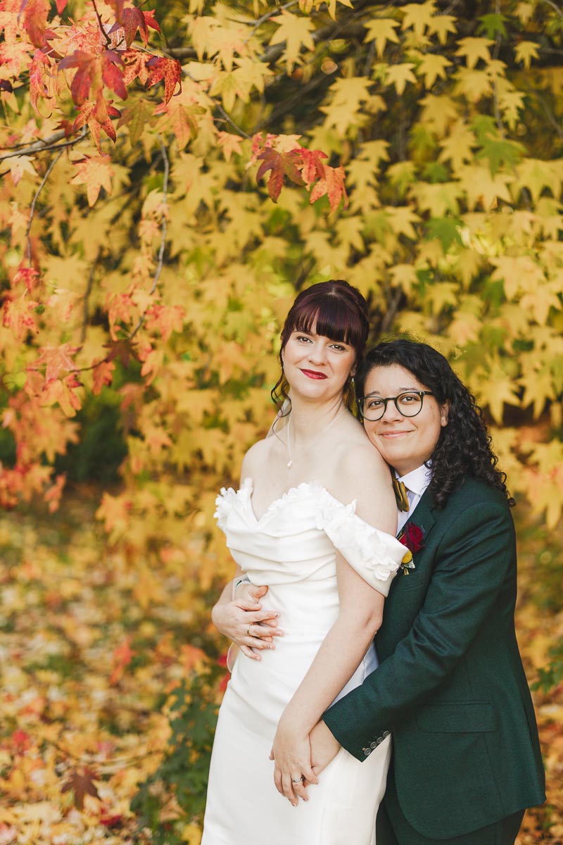 Same-sex wedding portrait of two brides standing together beneath autumn leaves in Dorset