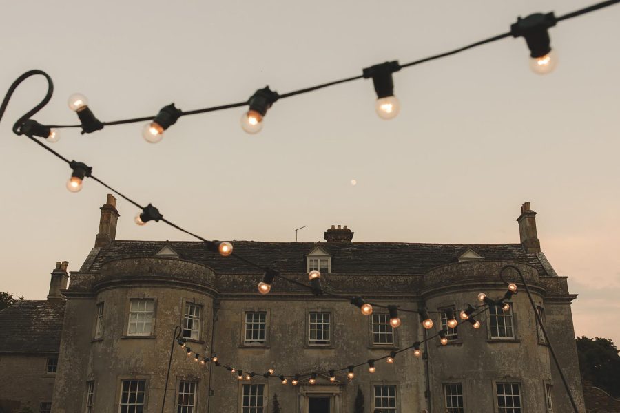 Smedmore House stone facade at dusk with warm festoon lights strung across the front and a crescent moon above