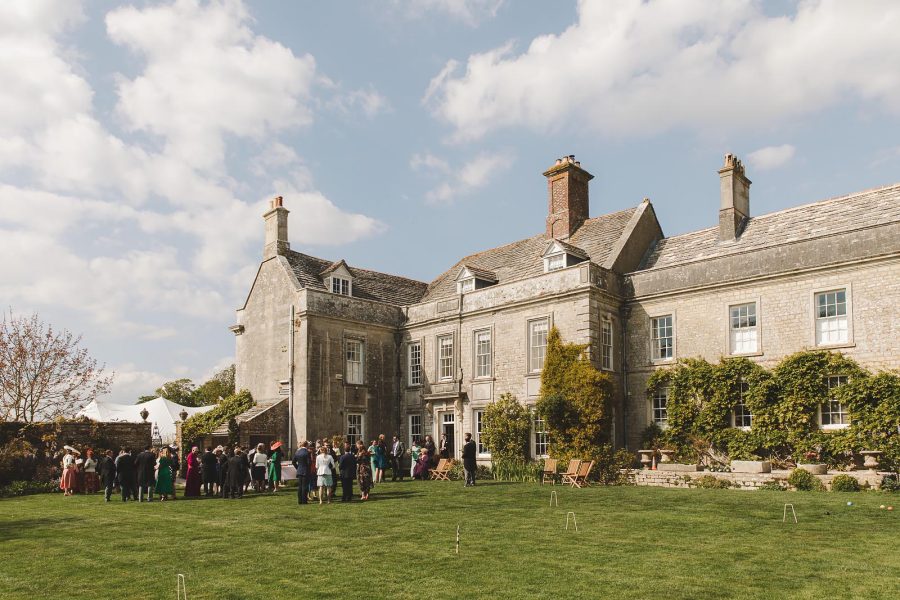 Guests arriving for a drinks reception on the sun-drenched lawns in front of Smedmore House with croquet set out on the grass