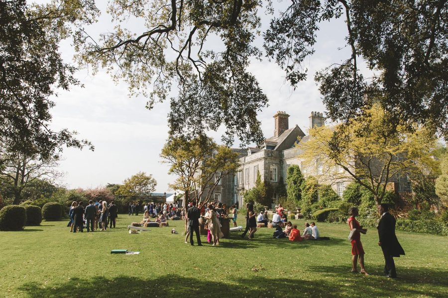 Wedding guests relaxing on the sunlit lawns at Smedmore House during the drinks reception with dappled light through the trees
