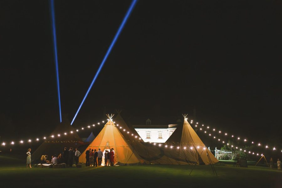 Smedmore House lit at night with illuminated tipi marquees and festoon lights and dramatic laser beams across the dark sky