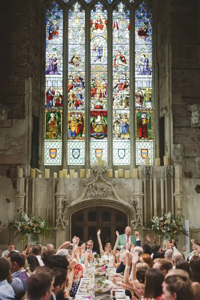 Guests raising their arms in celebration during wedding speeches in the Great Hall at Highcliffe Castle