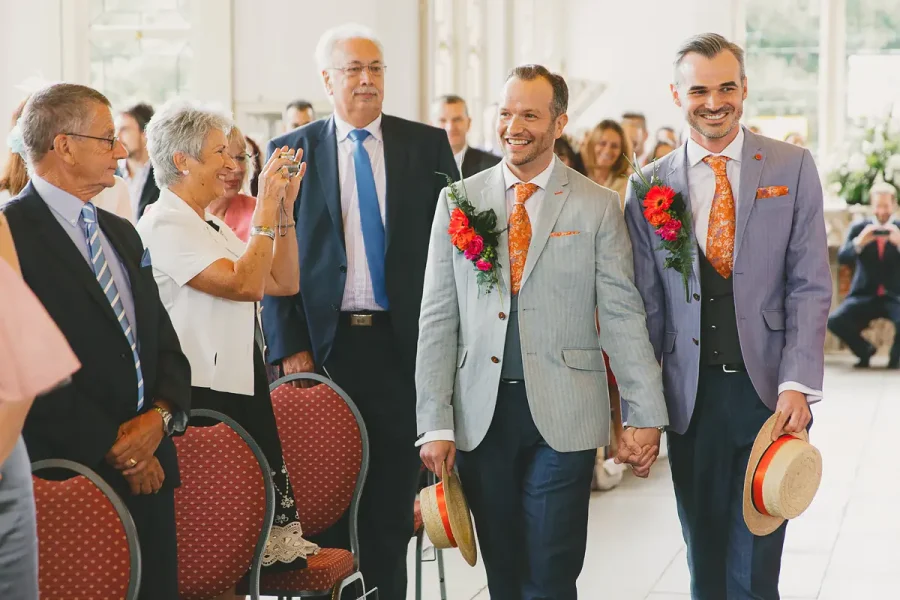 Two grooms walking hand in hand down the aisle in the Wintergarden at Highcliffe Castle
