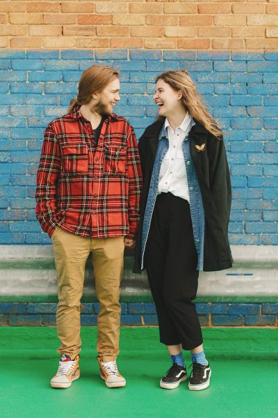 Couple laughing together against a colourful brick wall during an urban shoot