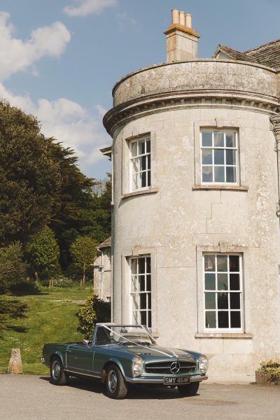 A vintage green Mercedes convertible parked beside the distinctive round corner tower of Smedmore House in the sunshine