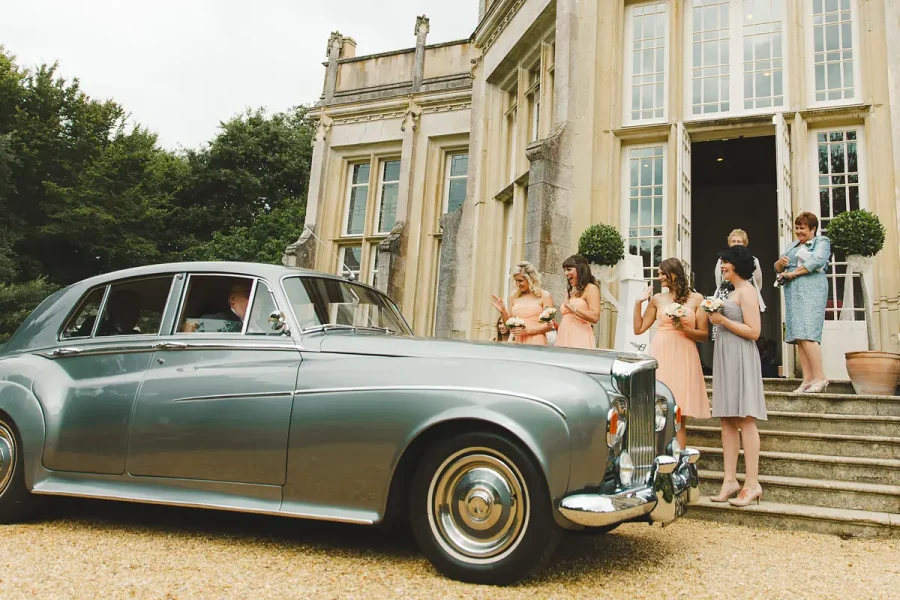 A vintage Rolls-Royce wedding car parked outside Highcliffe Castle with bridesmaids gathered on the steps