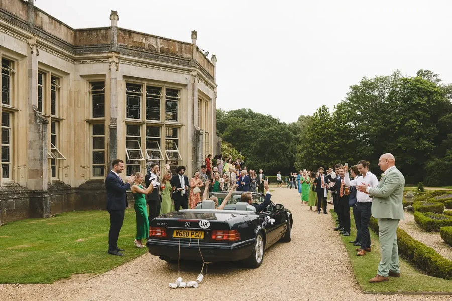 Black convertible wedding car parked by the terrace at Highcliffe Castle as guests watch from the gardens