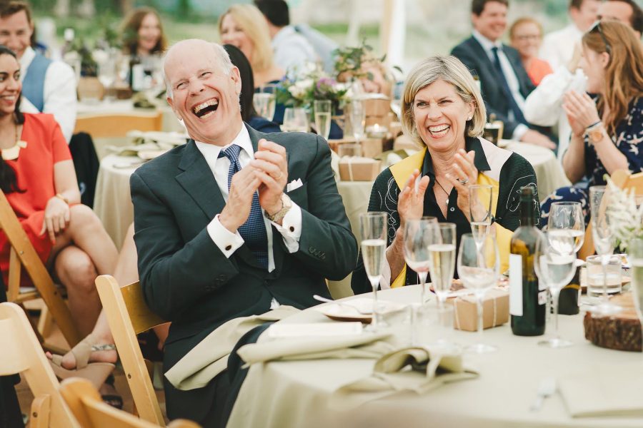 Couple laughing and clapping at the wedding breakfast table inside a white marquee at a Smedmore House reception