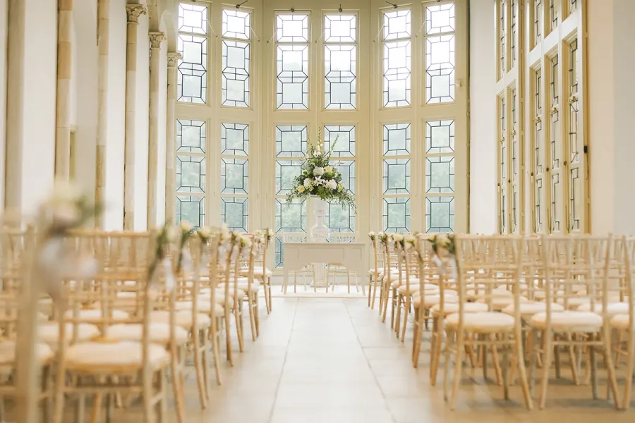 The Wintergarden at Highcliffe Castle set for a ceremony with chiavari chairs and a floral pedestal in the tall windows