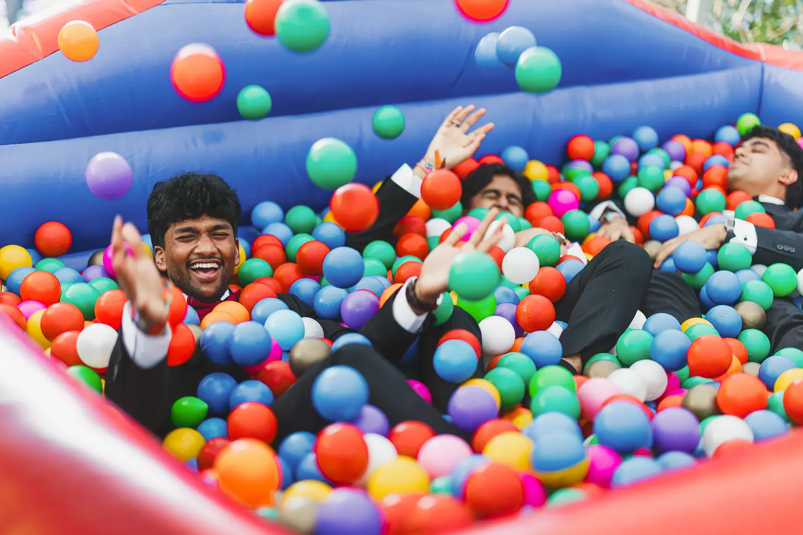 Guests in black tie laughing and throwing balls in a colourful ball pool at a surrealist-themed Cambridge May Ball