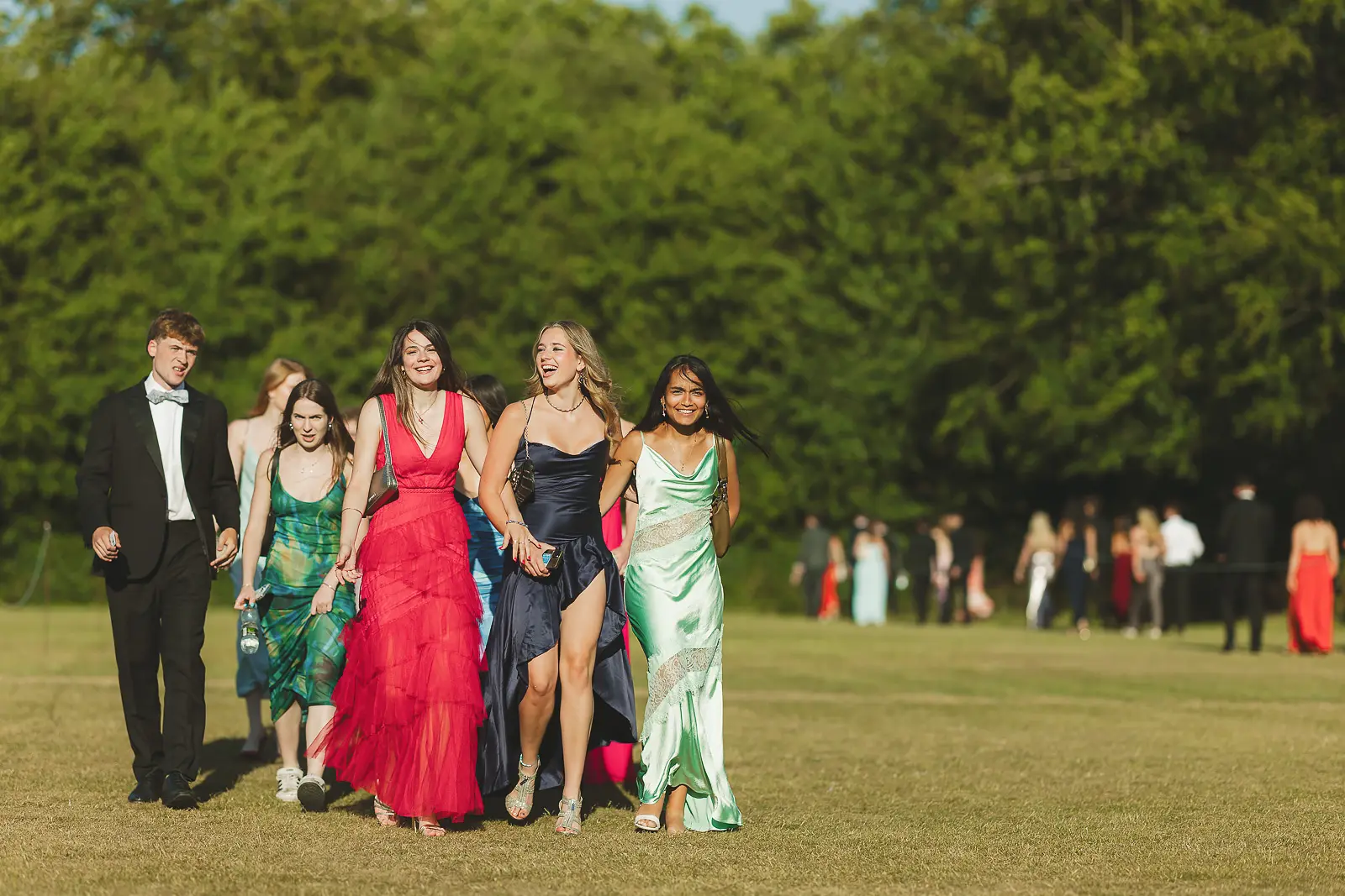 Group of guests in black tie and ball gowns walking across open lawns at a Cambridge May Ball